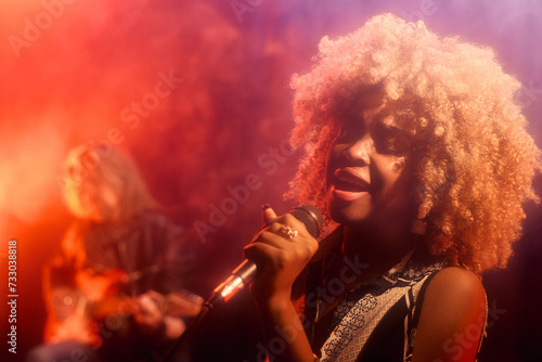 Portrait of young Black woman singing passionately to microphone on stage in hazy neon lights copy space