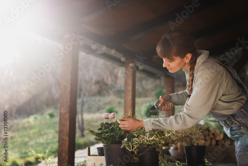 Young adult happy European woman on the terrace of cottage with pots of flowers and seedlings, spring gardening work © olezzo