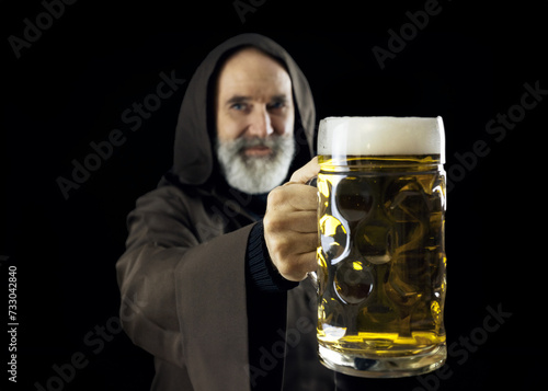 An amiable elderly friar, belonging to the Franciscan order, extends a massive mug brimming with fresh beer to the observer. 