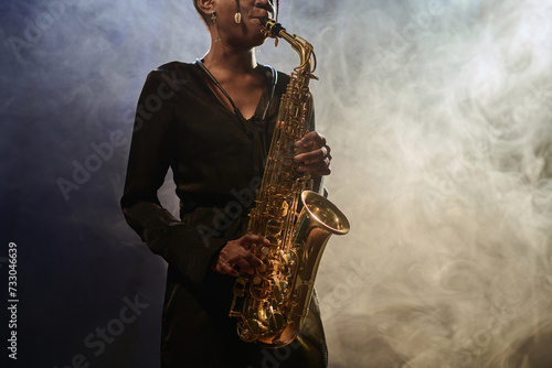 Cropped shot of elegant Black young woman playing saxophone in jazz music club with smoke effects copy space photo