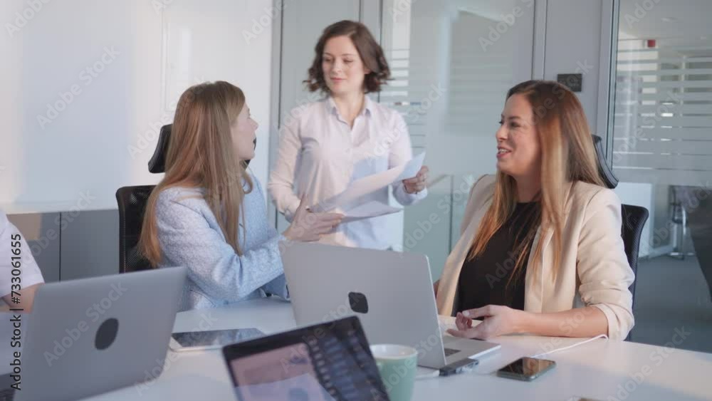 Female project manager giving meeting plan papers to team in conference room. Business employees of various ages teamwork and collaboration in boardroom Female project manager giving meeting plan papers to team in conference room. Business employees of various ages teamwork and collaboration in boardroom