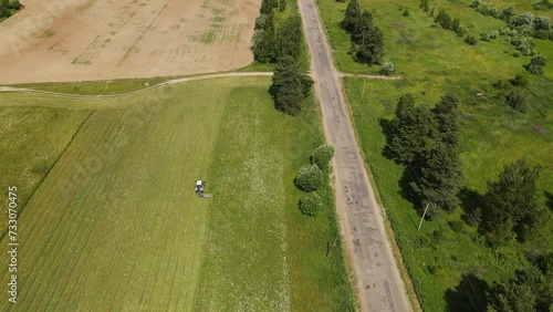 A tractor performs agricultural work on a green field covered with grass on a clear summer day, filmed from a drone