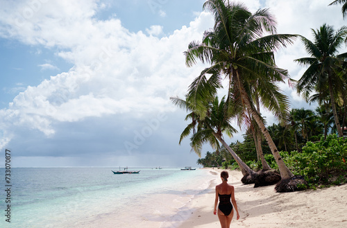 Vacation on the seashore. Back view of young woman walking away on the beautiful tropical white sand beach.