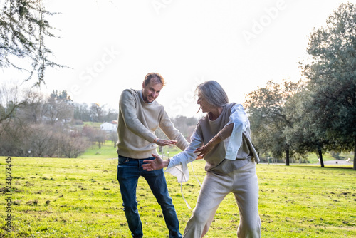 A woman and a middle-aged man practising neurodance in a green meadow in the nature of a park.