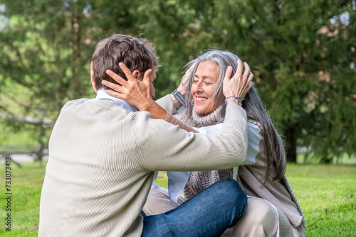 A man and a woman practising concentration exercises and spiritual connection sitting in a green meadow surrounded by trees in a park.