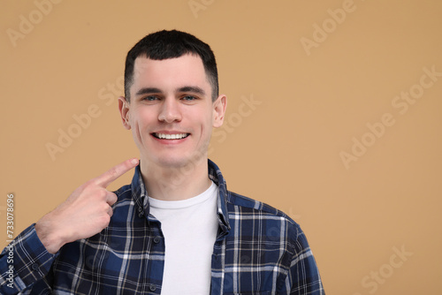Handsome young man showing his clean teeth on beige background, space for text © New Africa