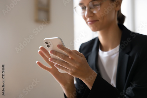 Positive young business professional woman using application on mobile phone, touching screen, typing, looking at screen, smiling, enjoying Internet communication. Close up of hands holding smartphone