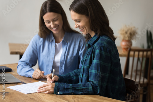 Cheerful female project partners signing contract  meeting at work table for negotiations  discussing partnership  project  investment  purchase  setting signature on paper agreement