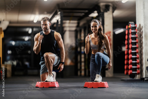 A fit couple is doing exercises for gluteus and legs in a gym.