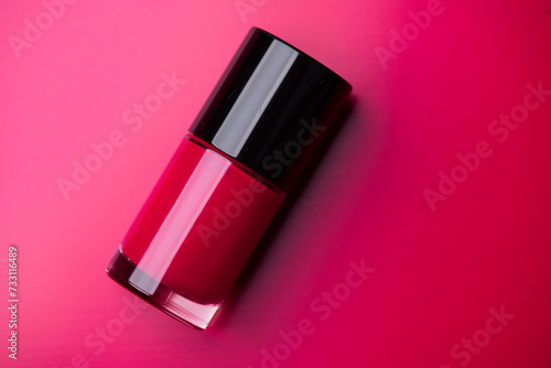 Red nail polish bottle over bright red background, top view. Gel nailpolish,  shellac UV, bottle with brush, varnish, manicure concept, Beauty salon. Glass bottle close up. Nail care product 