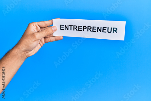 Hand of caucasian man holding paper with entrepreneur word over isolated blue background