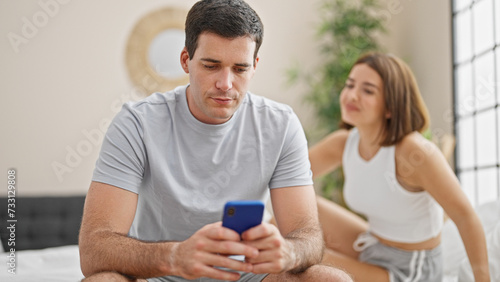 Beautiful couple sitting on bed with serious expression using smartphone at bedroom