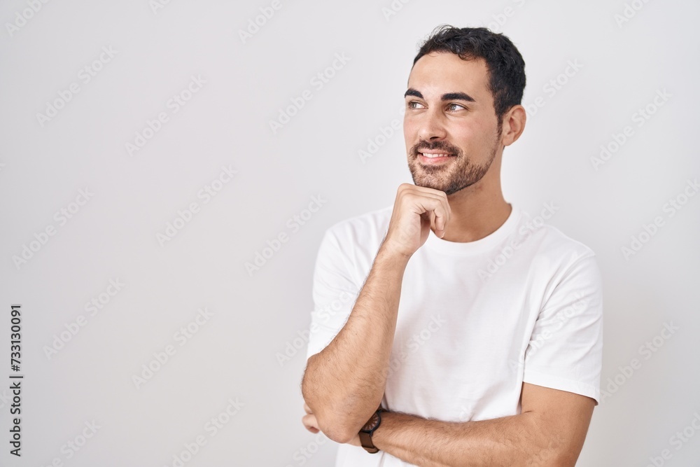 Handsome hispanic man standing over white background with hand on chin thinking about question, pensive expression. smiling and thoughtful face. doubt concept. Handsome hispanic man standing over white background with hand on chin thinking about question, pensive expression. smiling and thoughtful face. doubt concept.