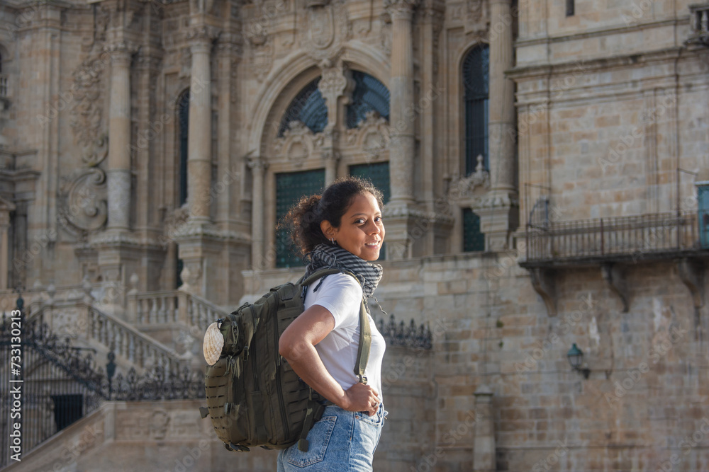 A female pilgrim on the Camino de Santiago, carrying a backpack adorned with a scallop shell, finishing her walk in front of the Cathedral of Santiago de Compostela