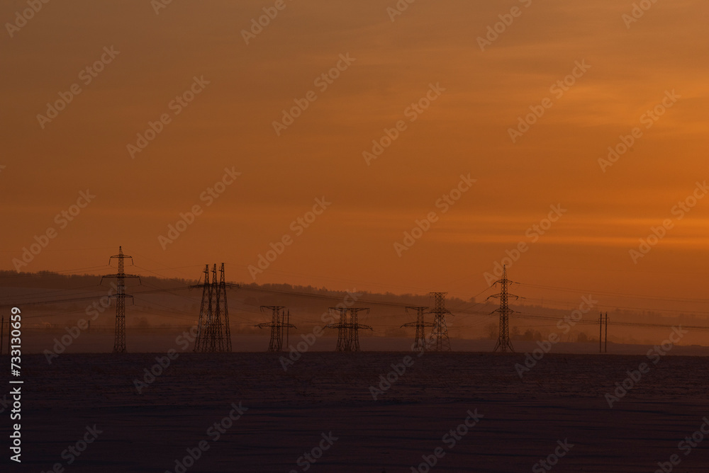 Russia. The South of Western Siberia. High-voltage metal structures against the background of a crimson dawn winter sky.