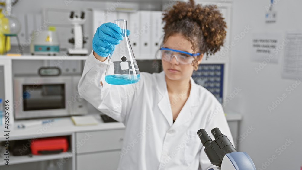 A young hispanic woman, with curly hair, examines a flask in a lab setting, illustrating science and healthcare. A young hispanic woman, with curly hair, examines a flask in a lab setting, illustrating science and healthcare.