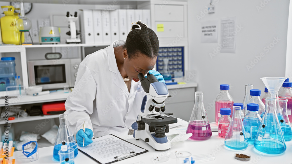 In the heart of the lab, attractive african american woman scientist seriously taking notes, working with microscope in bustling medical research center In the heart of the lab, attractive african american woman scientist seriously taking notes, working with microscope in bustling medical research center