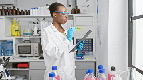 Passionate african american female scientist in lab gloves, fascinated by the power of medical research, deeply engrossed in taking notes at an indoor science laboratory photo