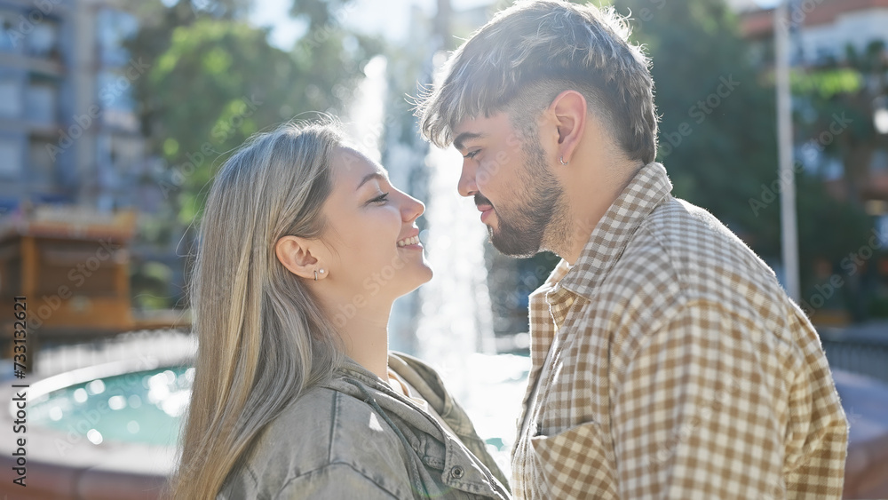 A smiling woman and man lovingly gaze at each other by a fountain in a sunny park. A smiling woman and man lovingly gaze at each other by a fountain in a sunny park.