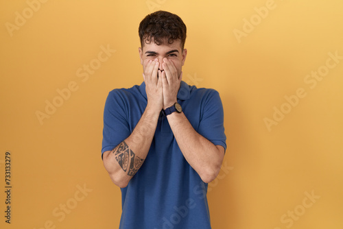 Foto Young hispanic man standing over yellow background laughing and embarrassed gigg