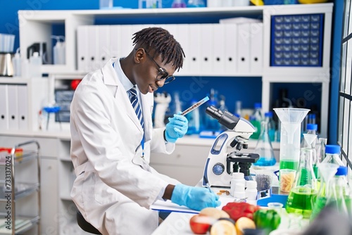 African american man scientist writing report holding test tube at laboratory