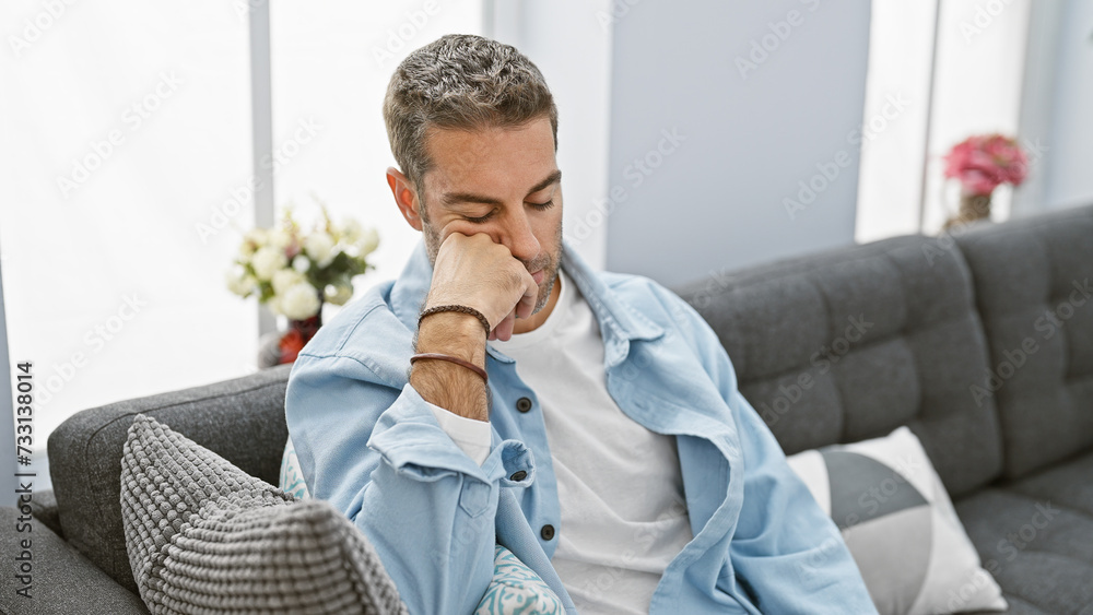 Thoughtful man contemplating while sitting on a gray sofa in a modern living room interior