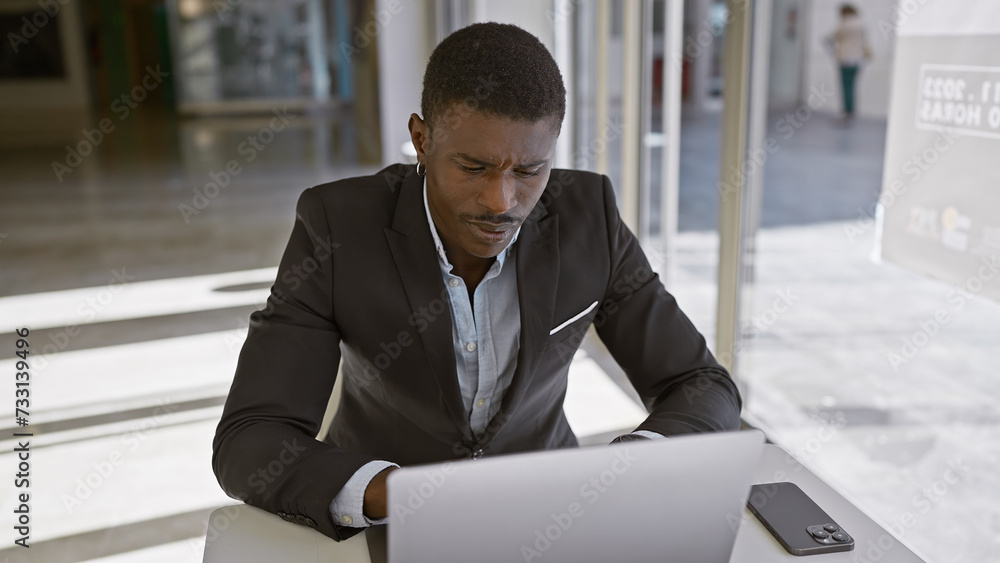 A focused african american man in a suit working on a laptop in a modern office environment, conveying professionalism and dedication. A focused african american man in a suit working on a laptop in a modern office environment, conveying professionalism and dedication.