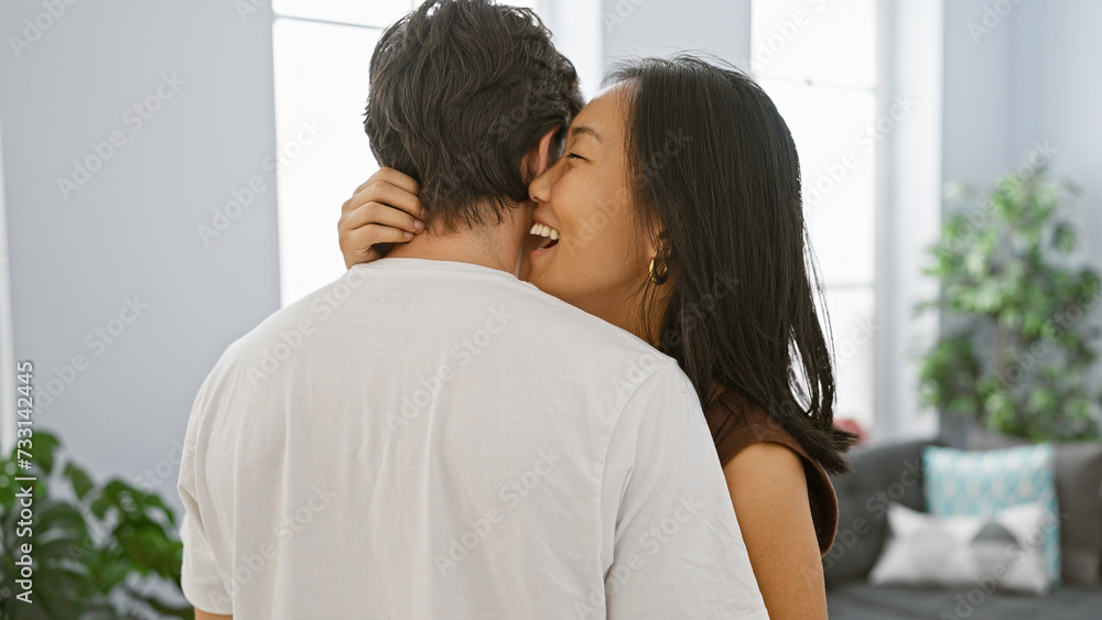 A smiling asian woman embracing a caucasian man in a bright, modern living room, expressing love and happiness. A smiling asian woman embracing a caucasian man in a bright, modern living room, expressing love and happiness.