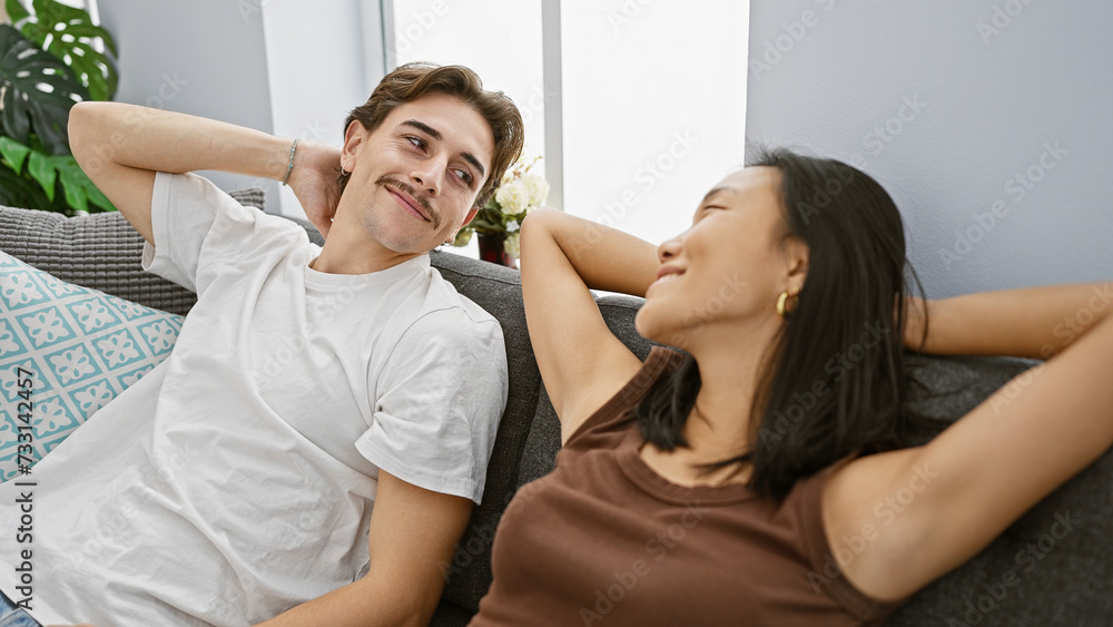 A relaxed interracial couple enjoy leisure time together in a modern living room, embodying love and comfort.