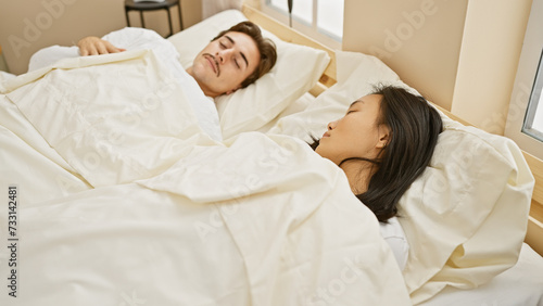 Interracial couple sleeping peacefully in a cozy bedroom, depicting a man and woman sharing a moment of rest at their home.