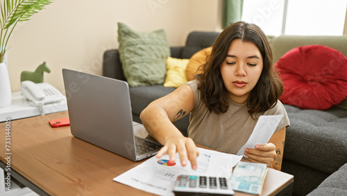 Foto Hispanic woman reviewing finances with calculator, bills, and laptop in home interior