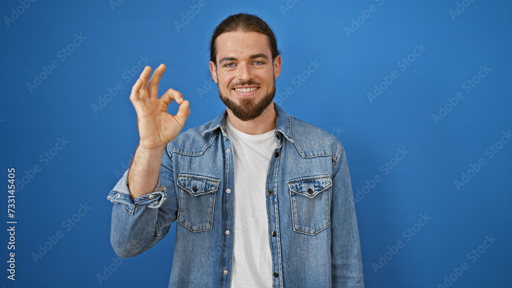 Young hispanic man smiling confident doing ok gesture over isolated blue background Young hispanic man smiling confident doing ok gesture over isolated blue background