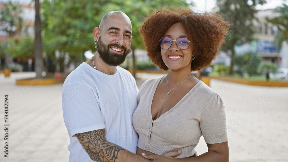 Obraz premium Beautiful couple, full of joy and positivity, hugging and sharing a sunny laugh in an outdoor park. casual, fun love, their confident smiles radiating happiness.