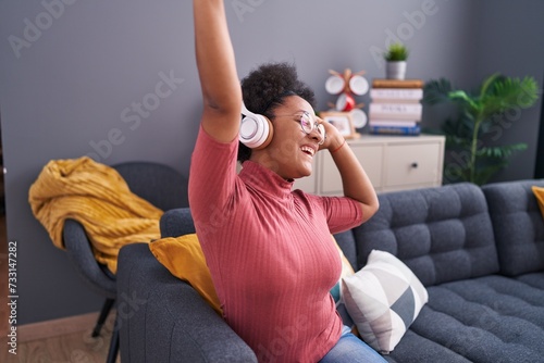 African american woman dancing and listening to music sitting on sofa at home