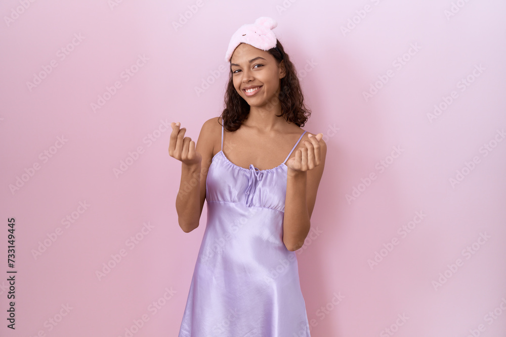 Young hispanic woman wearing sleep mask and nightgown doing money gesture with hands, asking for salary payment, millionaire business Young hispanic woman wearing sleep mask and nightgown doing money gesture with hands, asking for salary payment, millionaire business