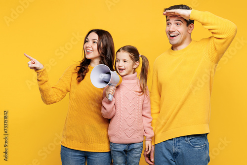 Young fun parents mom dad with child kid girl 7-8 years old wear pink casual clothes hold megaphone scream announces discounts sale point aside isolated on plain yellow background. Family day concept.