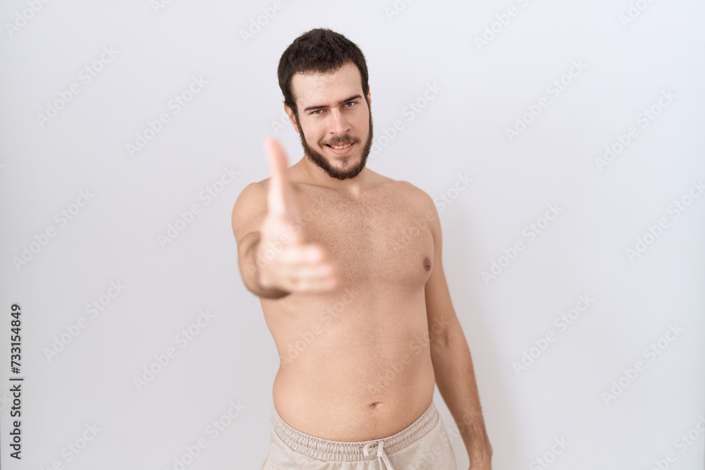 Young hispanic man standing shirtless over white background smiling friendly offering handshake as greeting and welcoming. successful business.