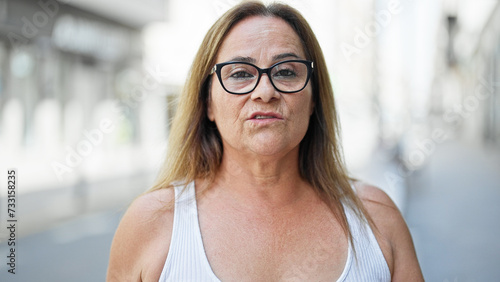 Middle age hispanic woman standing with serious expression speaking at street