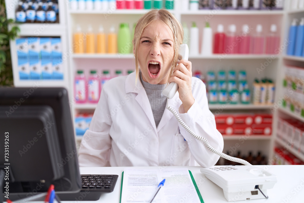 Young caucasian woman working at pharmacy drugstore speaking on the telephone angry and mad screaming frustrated and furious, shouting with anger. rage and aggressive concept. Young caucasian woman working at pharmacy drugstore speaking on the telephone angry and mad screaming frustrated and furious, shouting with anger. rage and aggressive concept.