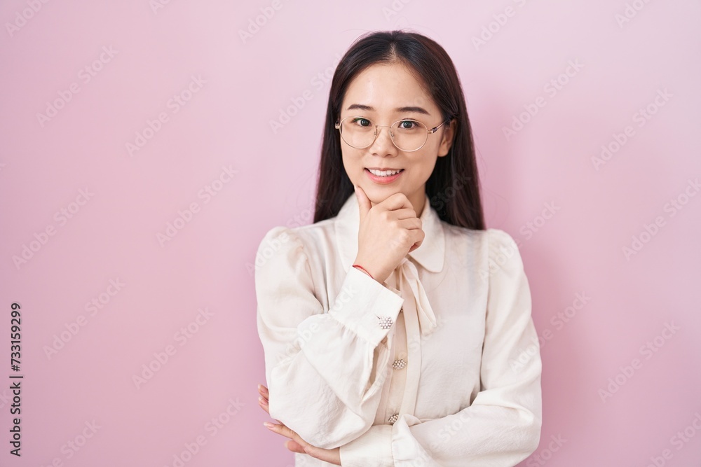 Young chinese woman standing over pink background looking confident at the camera smiling with crossed arms and hand raised on chin. thinking positive. Young chinese woman standing over pink background looking confident at the camera smiling with crossed arms and hand raised on chin. thinking positive.