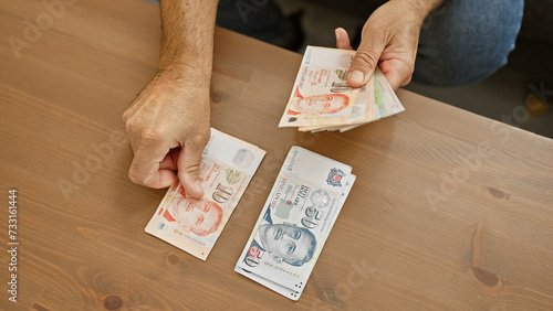 Man counting singaporean dollars at a wooden table indoors, portraying finance and domestic setting. photo