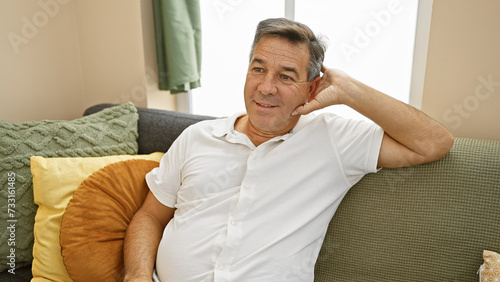 A relaxed middle-aged man sitting on a couch at home, with a content expression and comfortable modern decor.