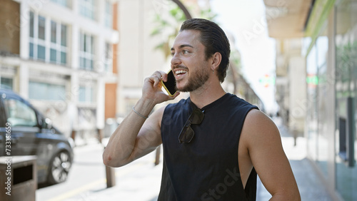 Young hispanic man talking on smartphone smiling at street