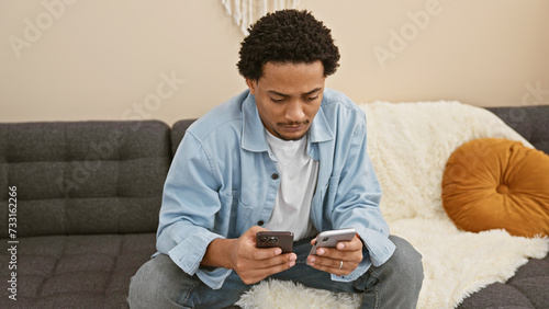 A young man using two smartphones while sitting in a modern living room. photo