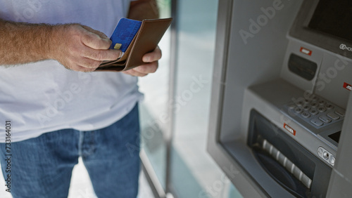 Handsome middle-aged caucasian man making a credit card transaction at a street atm. captivating portrait of an attractive adult male handling personal finances in an urban exterior.