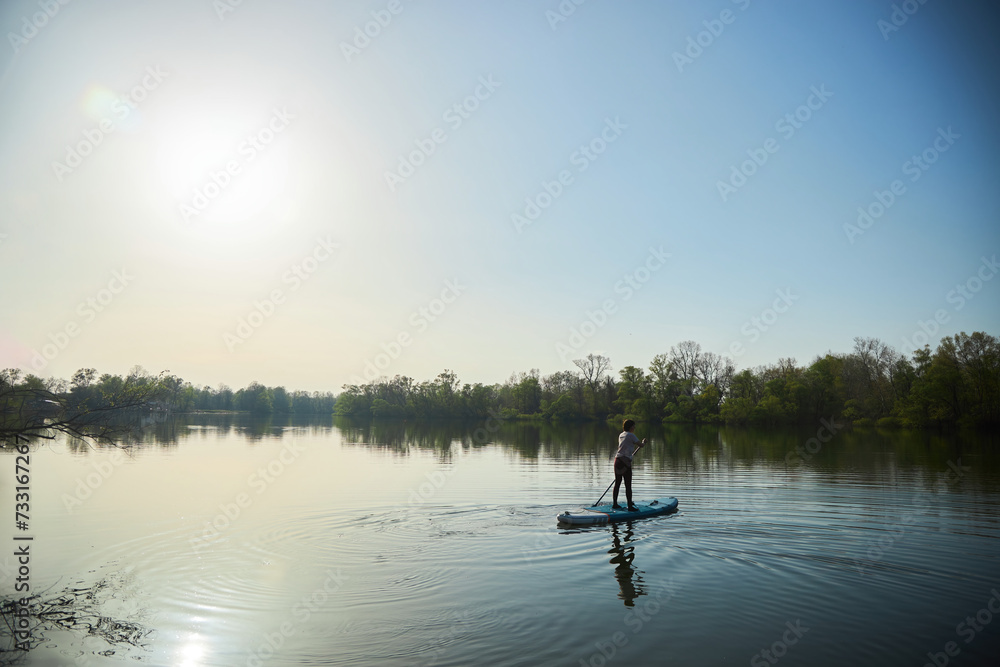 A woman swims on a sapboard on the lake. Water entertainment.