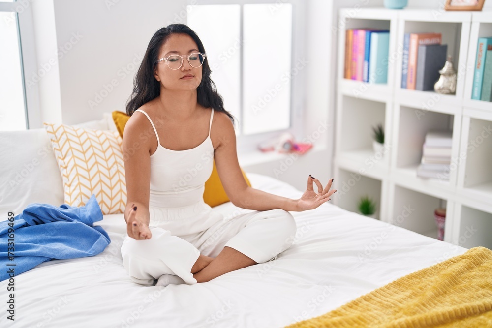 Young chinese woman doing yoga exercise sitting on bed at bedroom