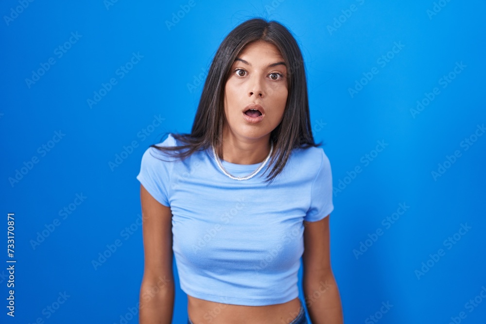 Brunette young woman standing over blue background afraid and shocked with surprise and amazed expression, fear and excited face. Brunette young woman standing over blue background afraid and shocked with surprise and amazed expression, fear and excited face.
