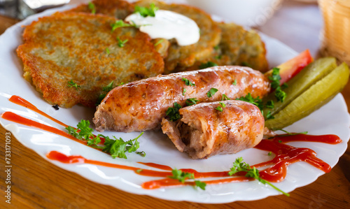 Potato pancakes with fried sausages on a white plate