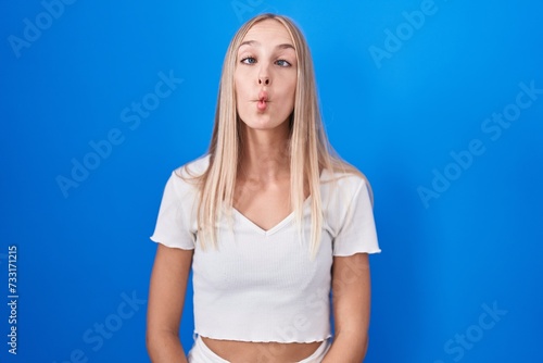 Young caucasian woman standing over blue background making fish face with lips, crazy and comical gesture. funny expression. © Krakenimages.com
